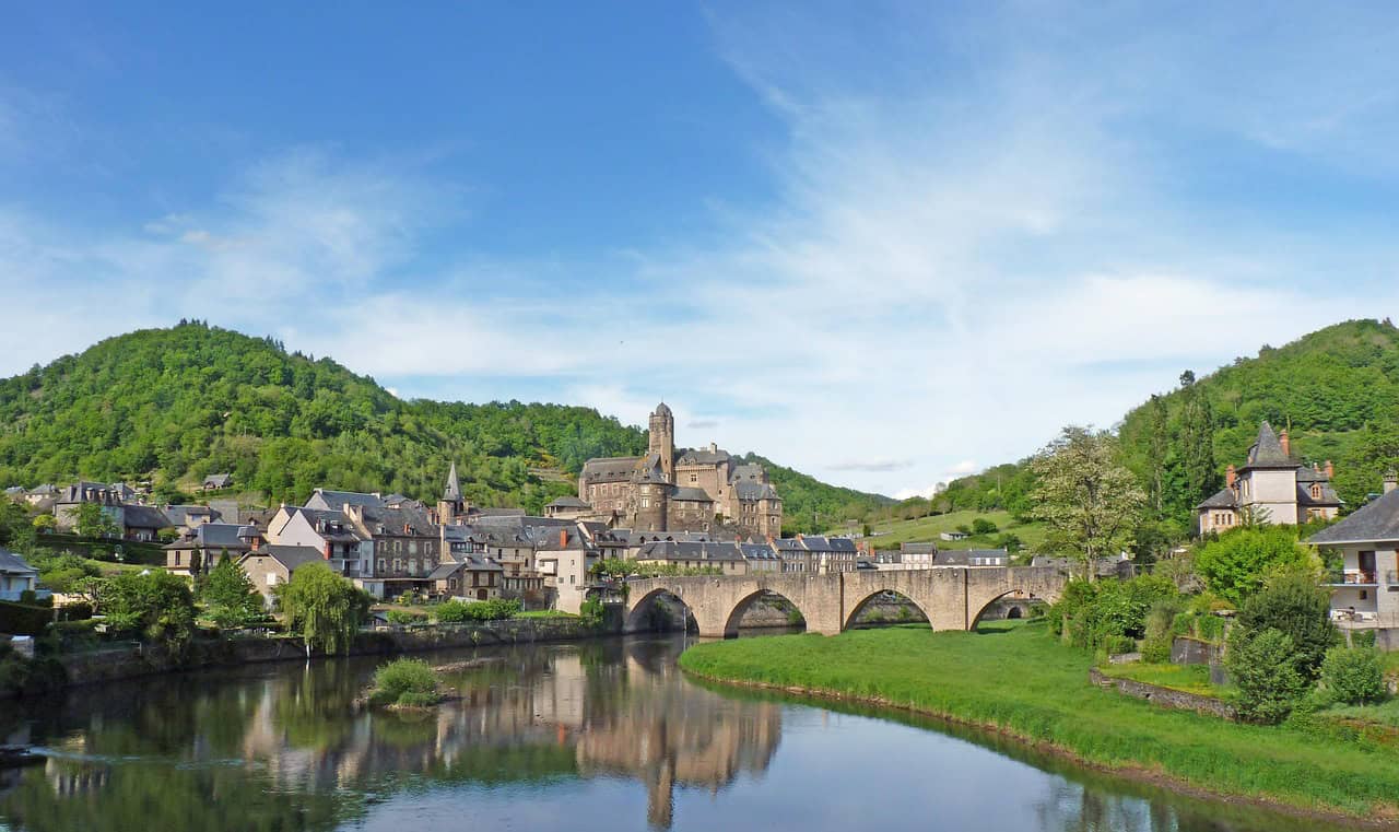 Festival de chorales en France. Une image d'une ville pittoresque avec un pont historique, entourée de montagnes verdoyantes, lors d'un festival chorale.